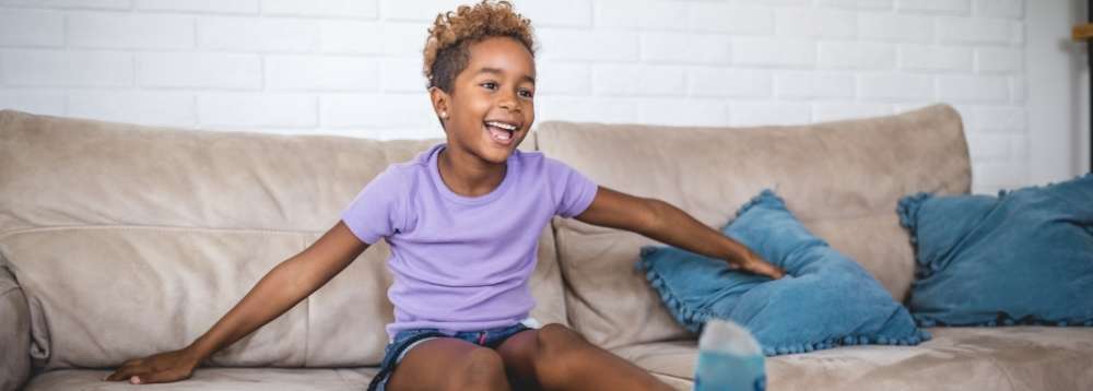 Picture of child sitting smiling on a sofa kicking their legs.