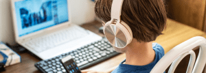 A young child using a laptop and a phone whilst wearing headphones. 