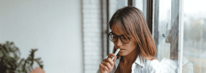 A woman wearing glasses, staring down in deep thought.