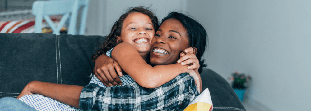 A female foster carer laughing and embracing her foster child.